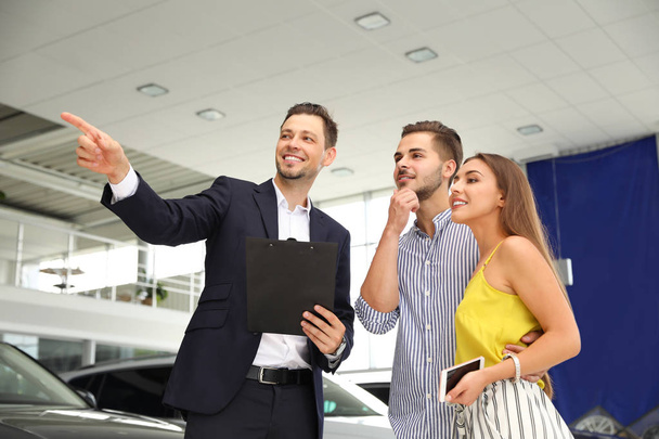 Young couple choosing new car with salesman in salon - Foto, Imagem