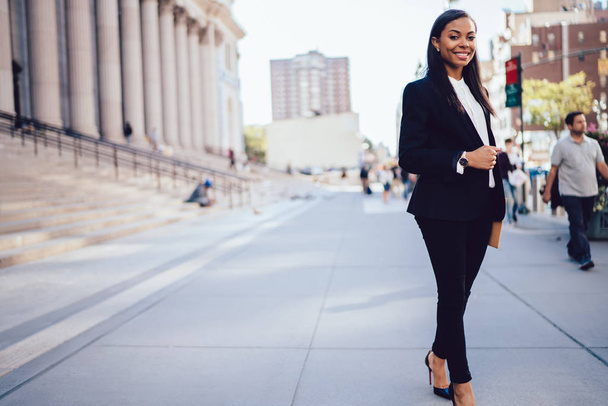 Full lengt portrait of successful african american businesswoman dressed in formal wear posing and smiling at camera in downtown.Prosperous student of faculty of law standing near university building - Foto, immagini