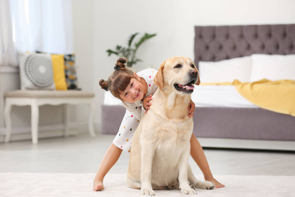 Adorable yellow labrador retriever and little girl at home - Foto, imagen