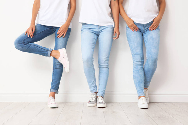 Group of young women in jeans near light wall - Foto, afbeelding