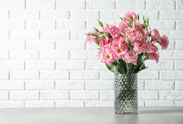 Vase with beautiful Eustoma flowers on table against brick wall - Фото, изображение