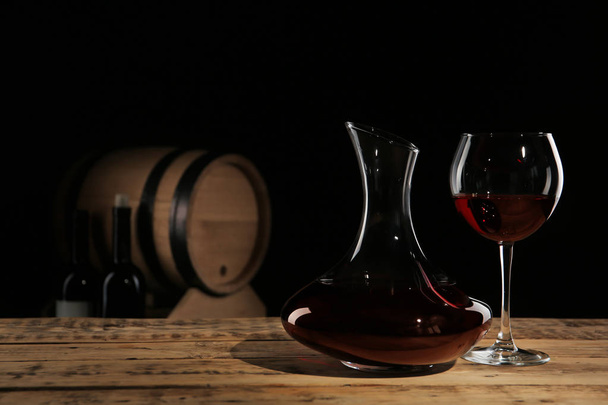 Κομψή καράφα και ποτήρι με κόκκινο κρασί στο τραπέζι ενάντια σε σκούρο φόντο - Φωτογραφία, εικόνα