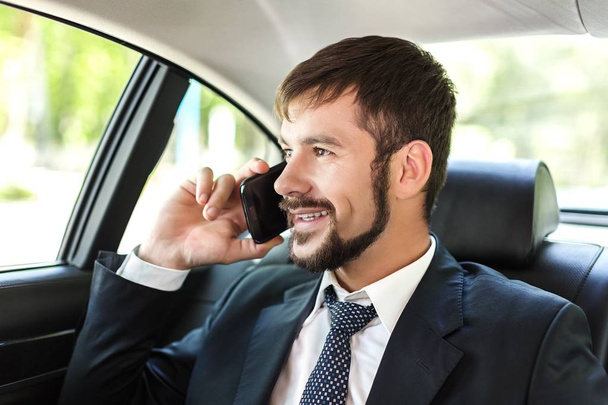 Elegant businessman traveling in luxury car, talking on mobile phone, smiling - Foto, Imagen
