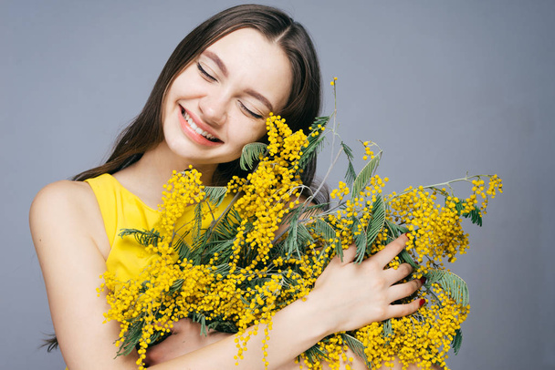 beautiful young girl smiling, enjoying the spring, holding a big bouquet of fragrant yellow mimosa - Foto, imagen