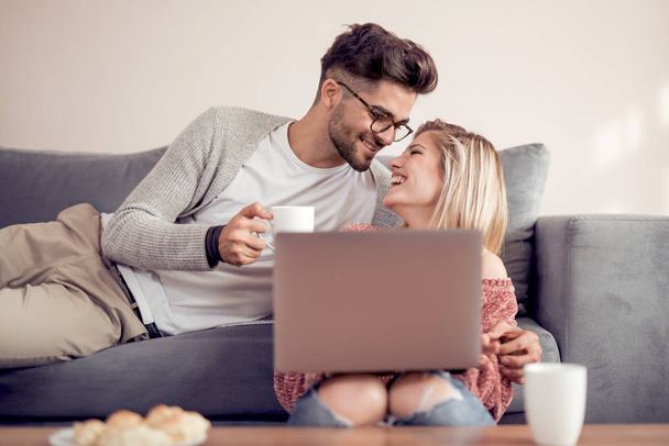 Couple assis sur le canapé, boire du café et utiliser un ordinateur portable à la maison
. - Photo, image