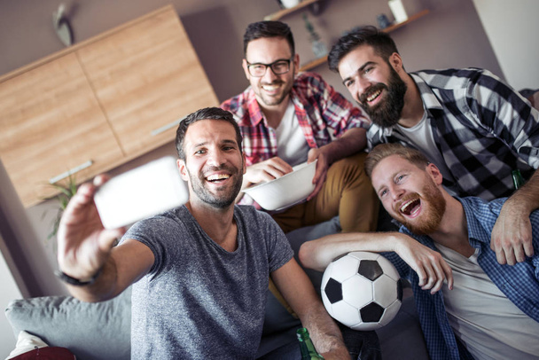 Весела група друзів розважається вдома, приймає селфі і дивиться футбол
. - Фото, зображення