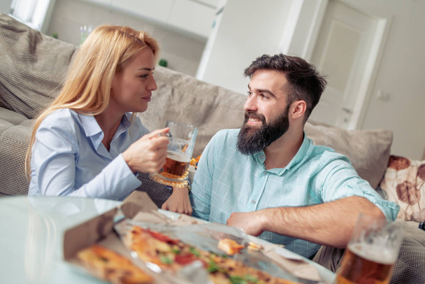 Jong (echt) paar hebben geweldige tijd thuis, eten van pizza en wijn drinken. - Foto, afbeelding