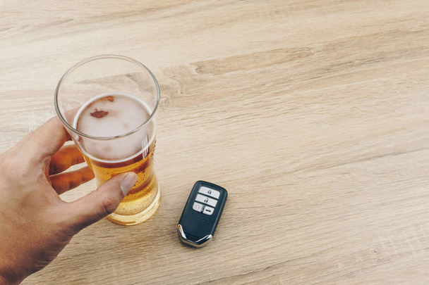 Czy nie pić i jazdy koncepcja, ręką, trzymając szklankę piwa i zdalny kluczyk na drewnianym stole - Zdjęcie, obraz