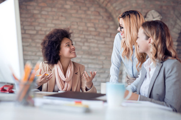 Drie vrouwen collega's maken grote zakelijk gesprek in moderne kantoren - Foto, afbeelding