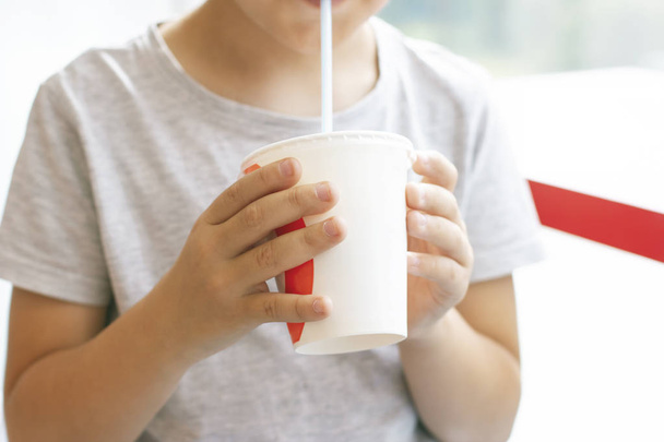 Мальчик 8 лет пьет коктейль из бумажной чашки, концепция быстрого питания
 - Фото, изображение