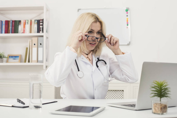 Здивований лікар в окулярах сидить на робочому столі
 - Фото, зображення