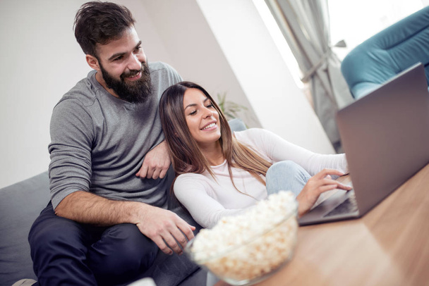 Young happy couple sitting on a sofa, using internet for online shopping. - Photo, Image