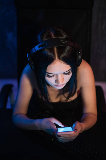 Vista superior de chica bonita relajándose en casa, ella está jugando música usando un teléfono inteligente y usando auriculares negros
. - Foto, imagen