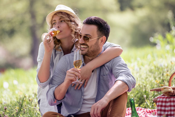 Feliz pareja atractiva sentados juntos y beber vino en la naturaleza
. - Foto, Imagen