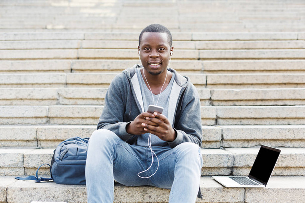 Αφρικανικός-Αμερικανός φοιτητής κάθεται σε σκαλοπάτια και τη χρήση του smartphone - Φωτογραφία, εικόνα