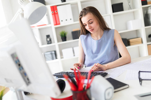 Beautiful young girl in the office sits at the table and prints on the keyboard. - 写真・画像