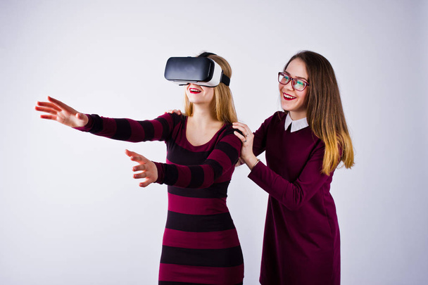 Две девушки в фиолетовых платьях примеряют очки виртуальной реальности в студии
. - Фото, изображение
