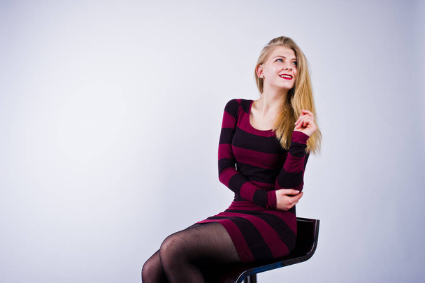 Portrait of a young woman in striped purple dress sitting on the chair in the studio. - Photo, image