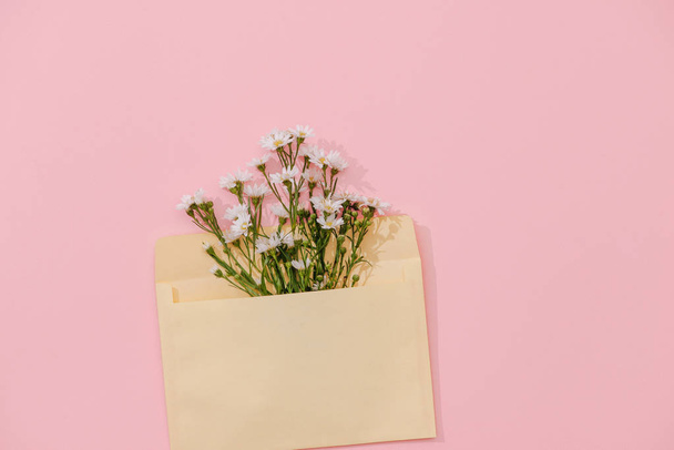 Geopende envelop met bloemen arrangementen op roze achtergrond, bovenaanzicht. Feestelijke begroeting concept - Foto, afbeelding