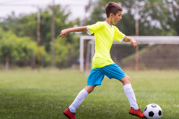 Poika potkii jalkapalloa urheilukentällä jalkapallo-ottelun aikana
 - Valokuva, kuva