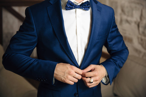 Primo piano di una cornice ritagliata di un uomo che abbottona la sua giacca elegante su un bottone, indossa una camicia bianca e un papillon, un uomo d'affari che indossa un anello d'oro al dito
 - Foto, immagini