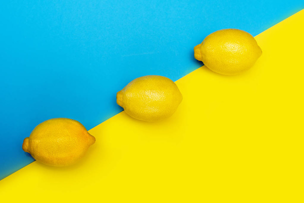 drei gelbe Zitronen hintereinander auf gelb-blauem Hintergrund. der Blick von oben. - Foto, Bild