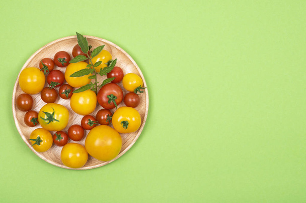Вид сверху на деревянную тарелку с красными и желтыми мелкими сортами помидоров на зеленом фоне. Вид сверху
. - Фото, изображение