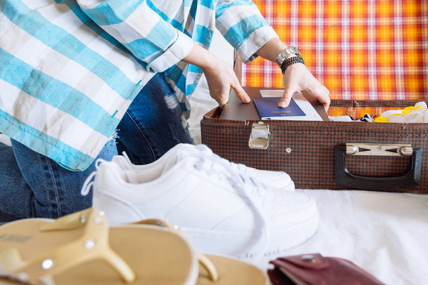 Frauenhände mit Armbanduhr packen Kleidung in Koffer. Reisekonzept. Kopierraum. Laptop-Brieftasche mit biometrischem Pass - Foto, Bild