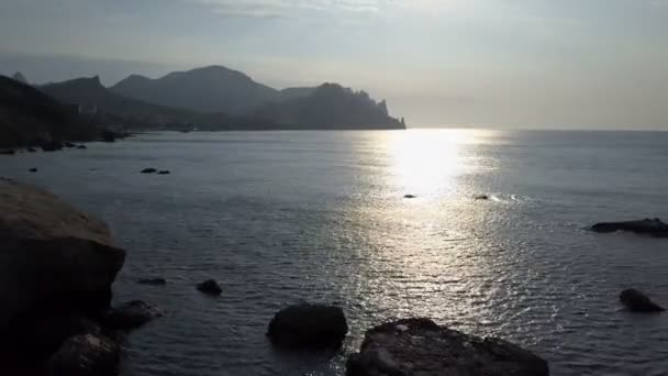 Πετώντας προς τα πίσω πάνω από την επιφάνεια της θάλασσας με βράχους και πέτρες στο sunrise. Βουνά, βράχια, πέτρες στα κύματα με και θάλασσα. Αεροφωτογραφία του Καρά Dag βουνό στην Κριμαία. - Πλάνα, βίντεο