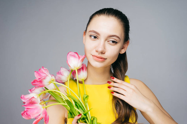 attractive young woman in yellow dress holds a bouquet of pink flowers in her hands, holiday - Foto, imagen