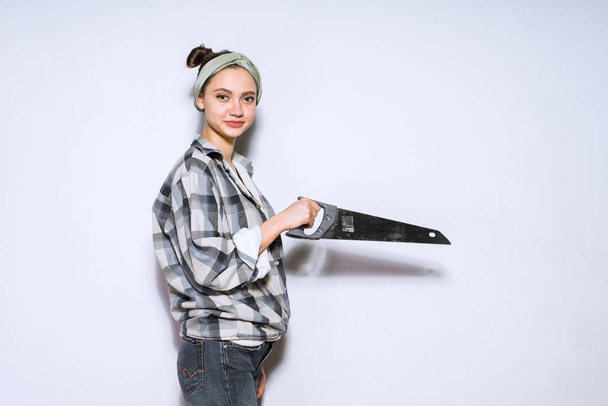 a young woman in a plaid shirt doing repairs, holding a sharp metal saw - Фото, изображение