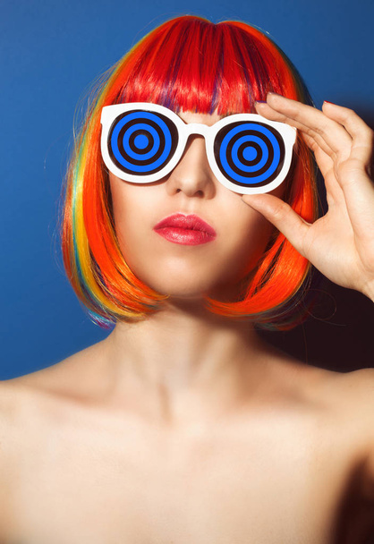 Young woman in colorful wig and white sunglasses on blue background - Φωτογραφία, εικόνα