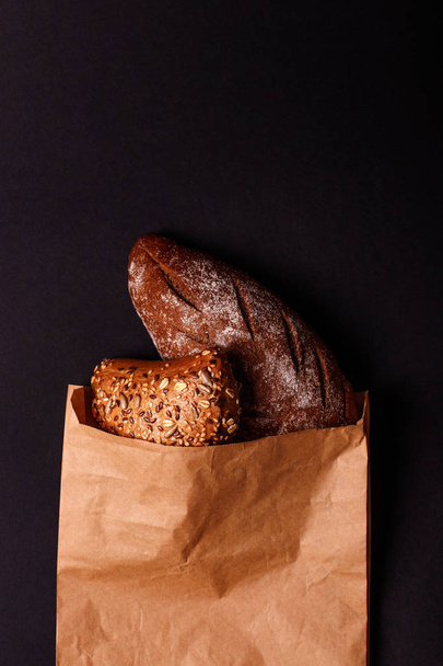 Žitný chléb a chutná buchta v papírový sáček izolované na černém pozadí. Místo textu - Fotografie, Obrázek