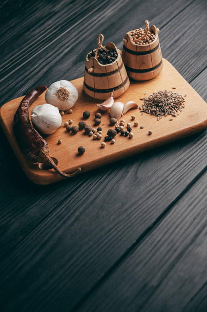 Gewürze: Chili, schwarzer Pfeffer, Knoblauch, Kreuzkümmel, Koriander, Paprika liegen auf einem braunen Holzbrett auf einem schwarzen Tisch. Platz unter dem Text - Foto, Bild