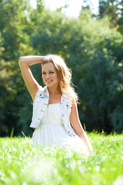 Young beautiful blonde woman in white dress sitting on green grass in the summer park - Fotografie, Obrázek
