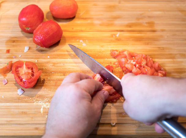 Man cutting and chopping tomatoes with knife on wooden plate - Valokuva, kuva