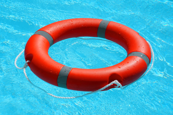Punainen pelastusrengas kelluu sinisellä vedellä. Elämänrengas kelluu aurinkoisen sinisen veden päällä. Life rengas uima-altaassa - Valokuva, kuva