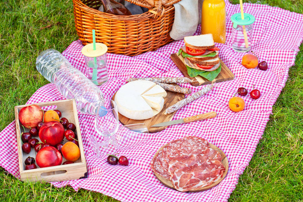 Picnic basket with different snacks on the green grass in the garden - Photo, Image