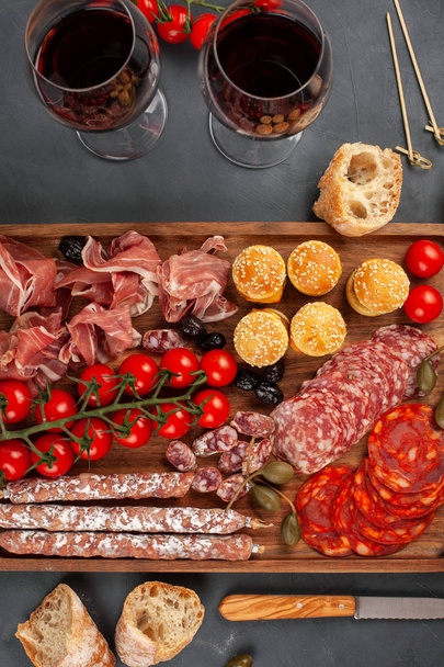 Appetizers table with differents antipasti, cheese, charcuterie, snacks and wine. Mini burgers, sausage, ham, tapas, olives, cheese and baguette over grey concrete background. Top view, flat lay - Zdjęcie, obraz