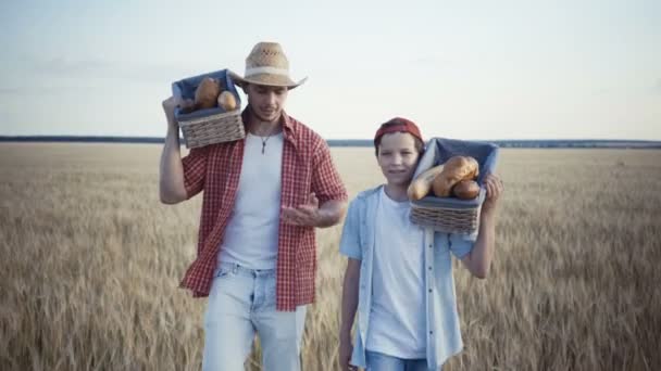 Mladí zemědělci jsou pěší podél pole pšenice s pletené košíky - Záběry, video