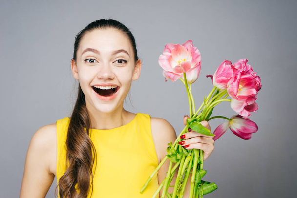 cheerful laughing girl in yellow dress holds a bouquet of pink flowers, happy spring - Fotografie, Obrázek