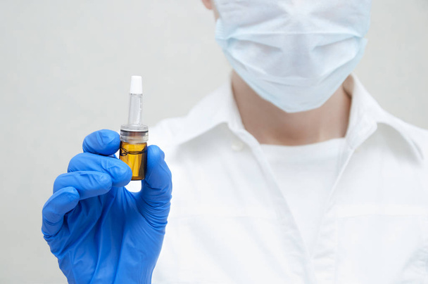 Médecin cosmétique dans le masque garde dans sa main dans des gants bleus ampoule avec de la drogue sur fond blanc gros plan
 - Photo, image