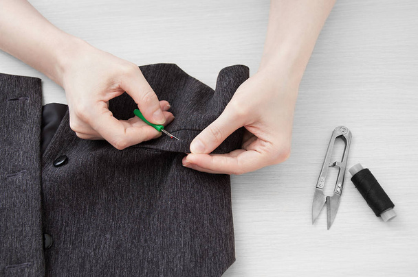 Girl tailor rips thread on a gray waistcoat. View from abov - Φωτογραφία, εικόνα