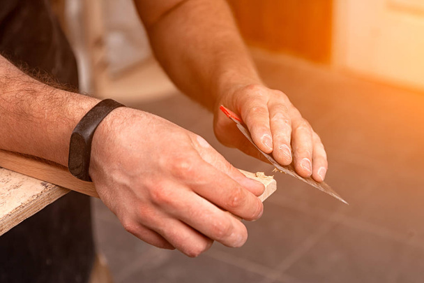 Yakın çekim A genç erkek marangoz mor bir gömlek fazla ambalaj kaldırır ve ahşap bir kapı atölye bir spatula ile donatıyor - Fotoğraf, Görsel