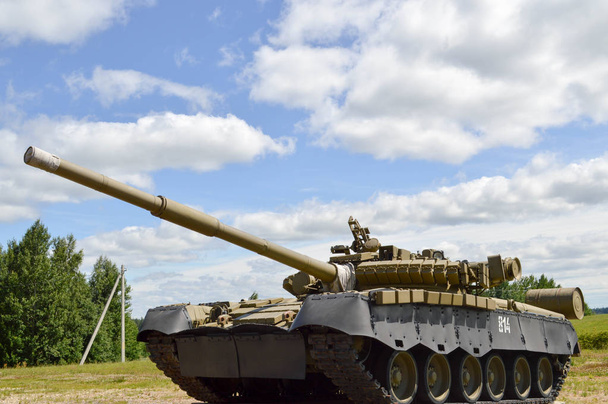 ein großer grüner militärischer Panzer aus Metall, gepanzert mit tödlichem Eisen, russisch-syrischer Kampfpanzer mit Geschützturm und einer Gans wird vor blauem Himmel und Wolken außerhalb der Stadt geparkt - Foto, Bild