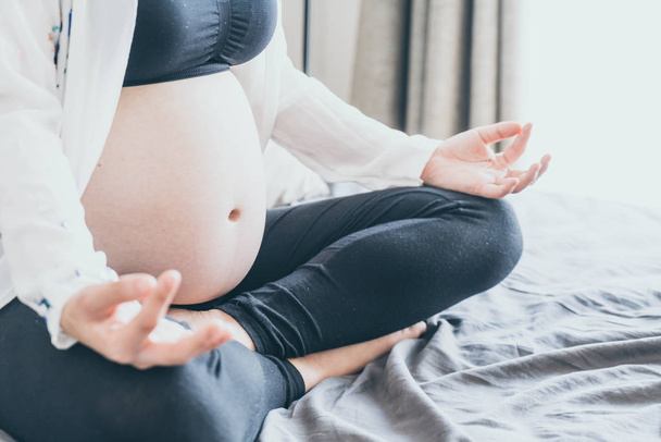 Young beautiful Asian pregnant woman meditating or doing yoga exercise at home. Relaxation yoga lotus pose. - selective focus point and vintage  style - Photo, Image