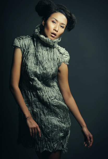 Beauty and fashion concept: young Asian fashion model in grey dress against black background - Foto, imagen