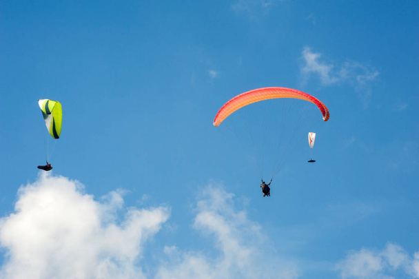 Три парапланери летять на блакитному небі на тлі хмар. Параглінг в небі в сонячний день
. - Фото, зображення
