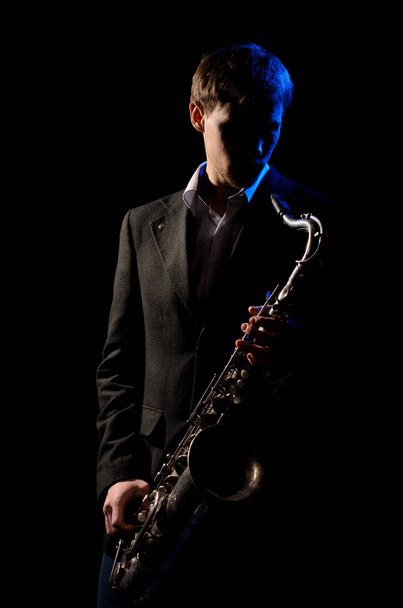 Saxophonist, illuminated by blue and white light, plays a melody on a black background - Photo, Image