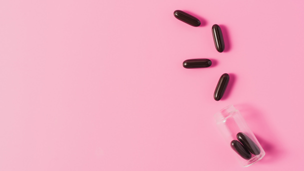 top view of black medical capsules spilled from bottle on pink - Foto, Imagen